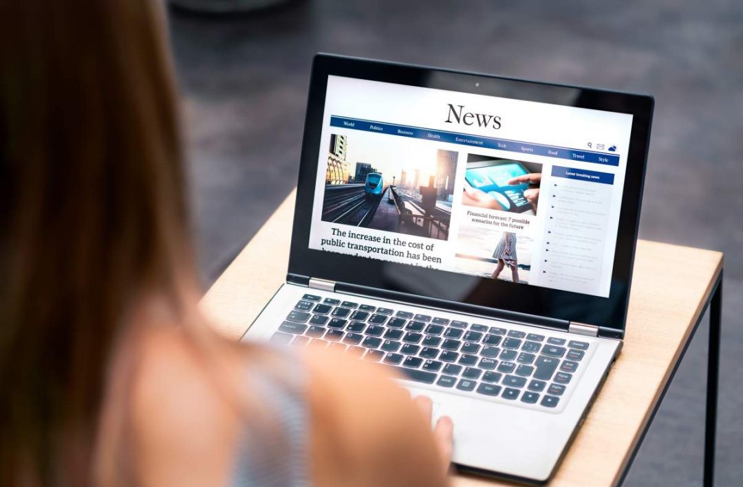 Blick über die Schulter einer Frau, die die Schlagzeilen und Überschriften auf einer News-Seite auf dem Laptop ansieht